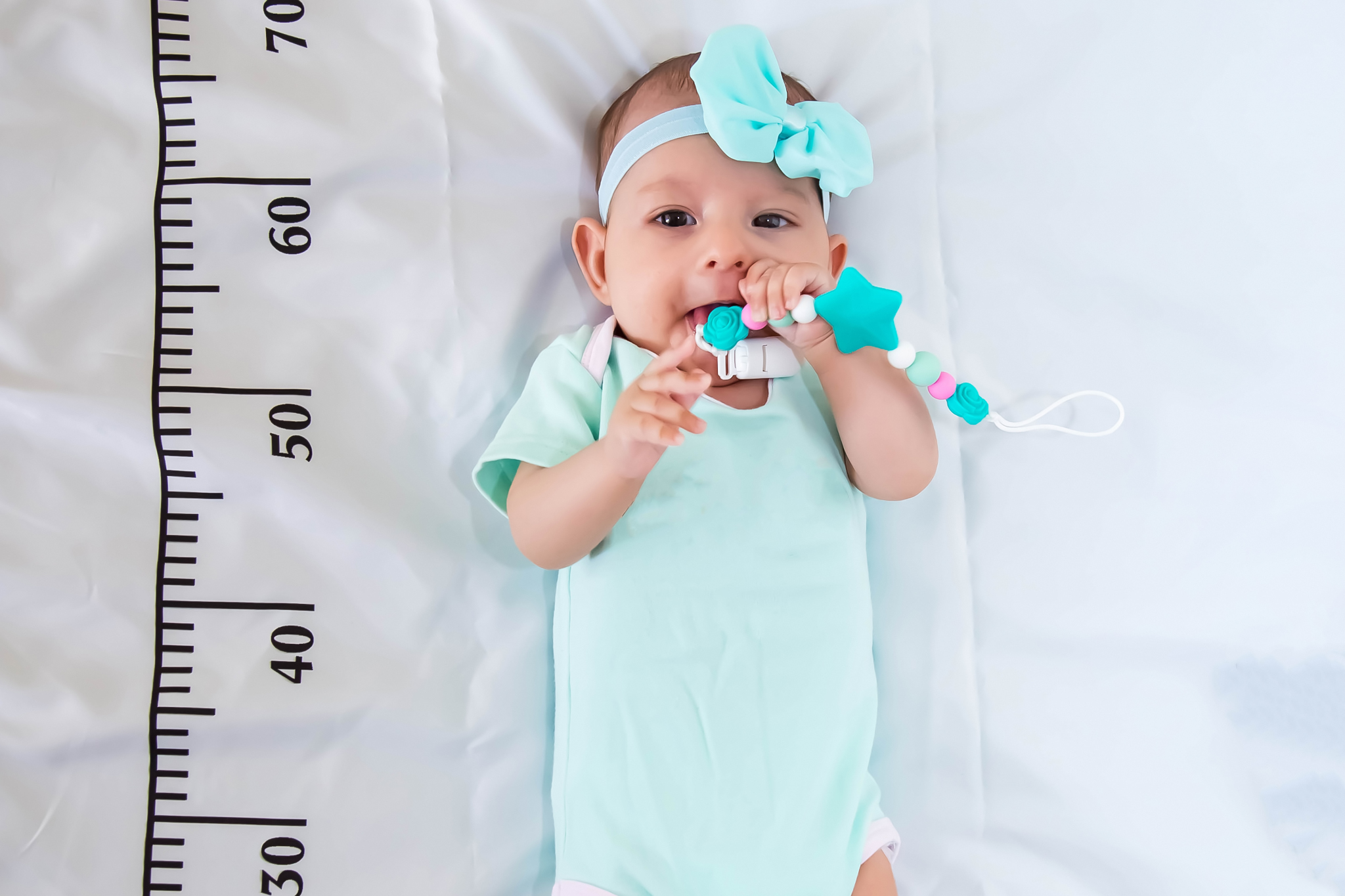 A three month baby girl in mint green clothes lying on a bed on
